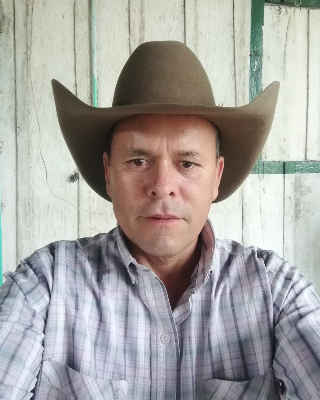 Cliente con sombrero café y camisa de cuadros, frente a una pared de madera rústica
